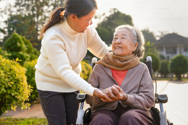 closeup happy grandma on wheelchair talking with carer in the garden in the morning sun