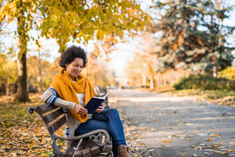 Young African American woman reading a book in the public park.